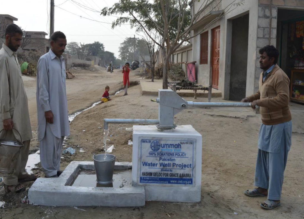 Community members gather around a newly installed water pump in Pakistan, part of the Grace and Nabra water well project, promoting access to clean water.