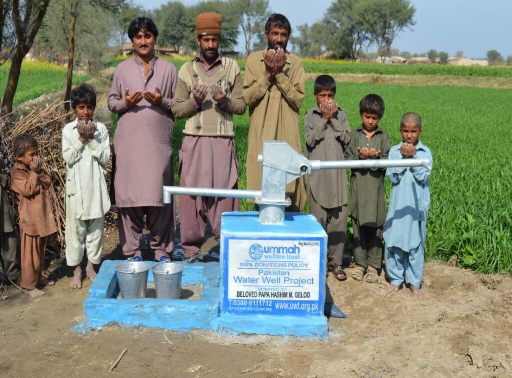 Villagers stand by a newly installed water well in Pakistan, showcasing community effort in the Ummah Welfare Project for access to clean water.