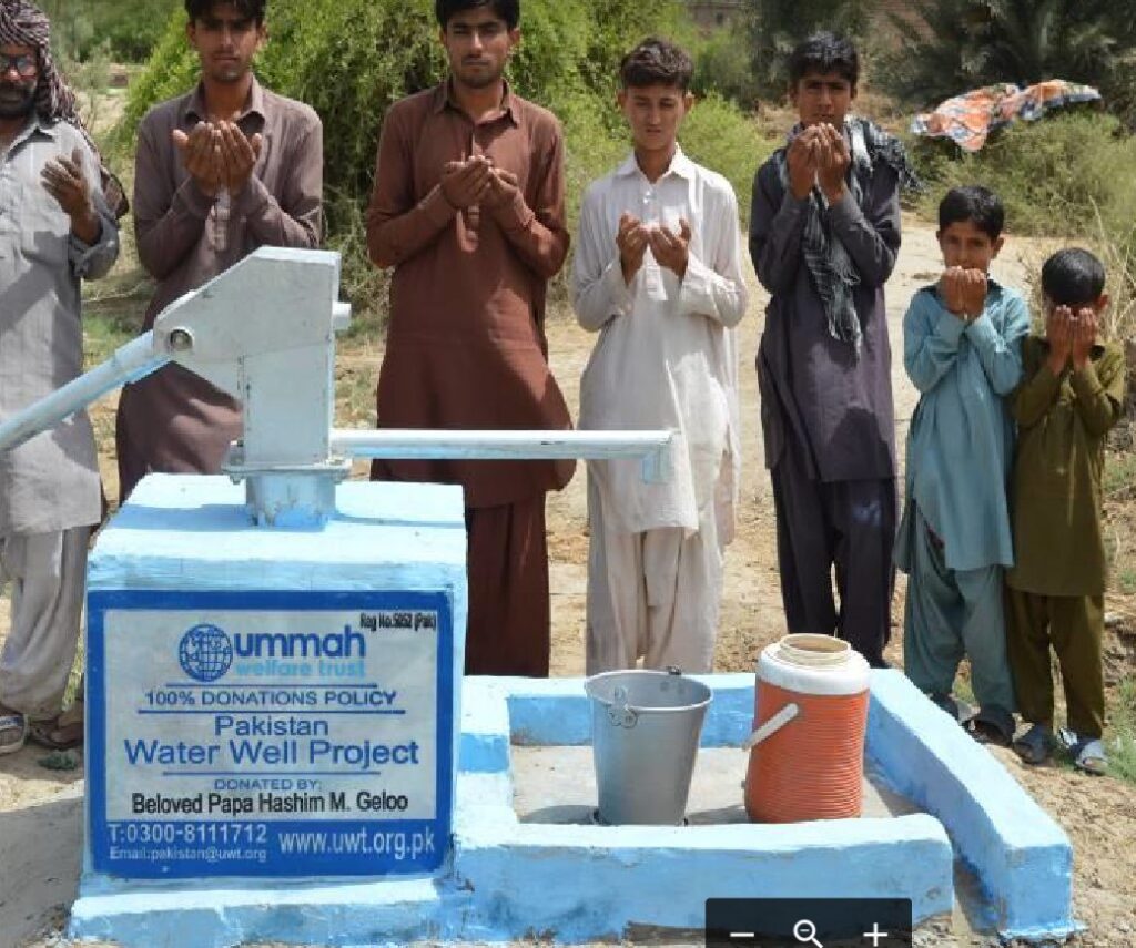 Children and men gather around a newly installed water well in Pakistan, celebrating the donation from the Ummah Welfare Trust for clean water access.